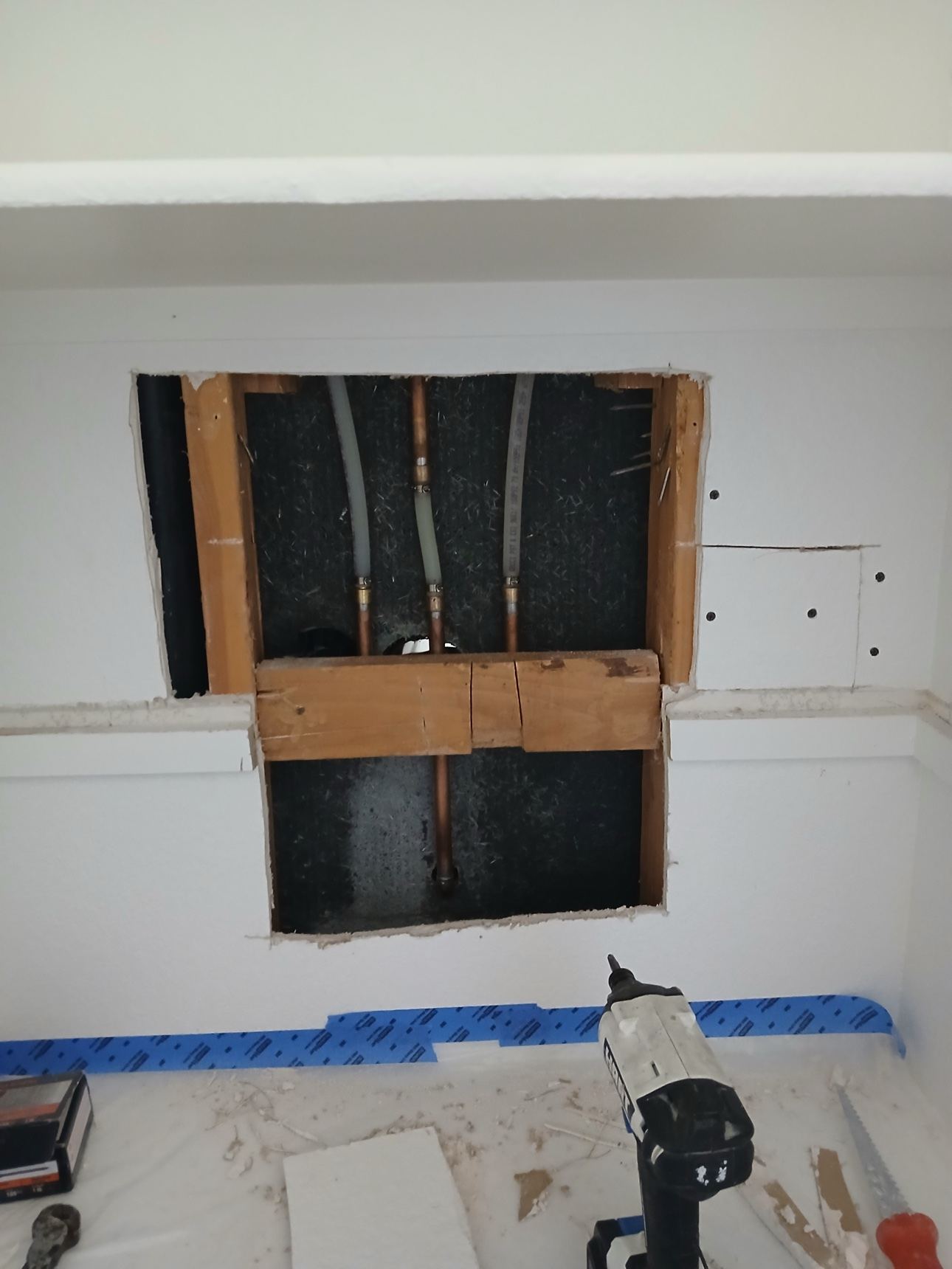 Drywall cut away exposing studs and water lines during repair