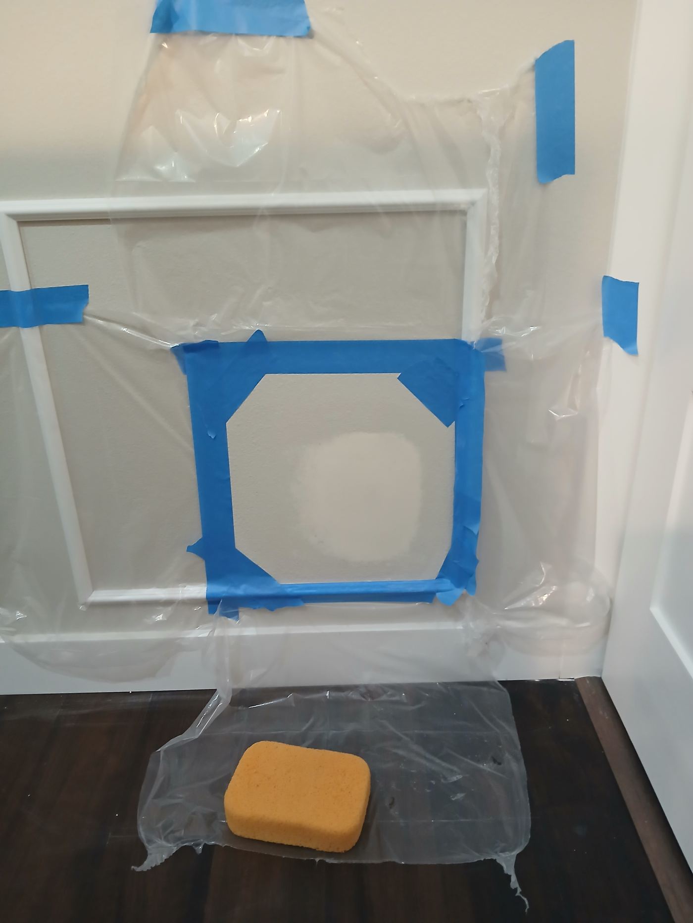 Door with patched area masked in plastic sheeting and blue painter's tape, prepped for texture work on a Wall Repair Pros job